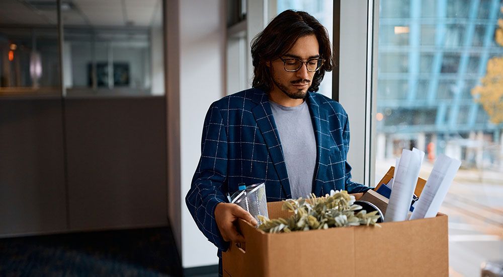 A man is holding a cardboard box filled with his belongings.