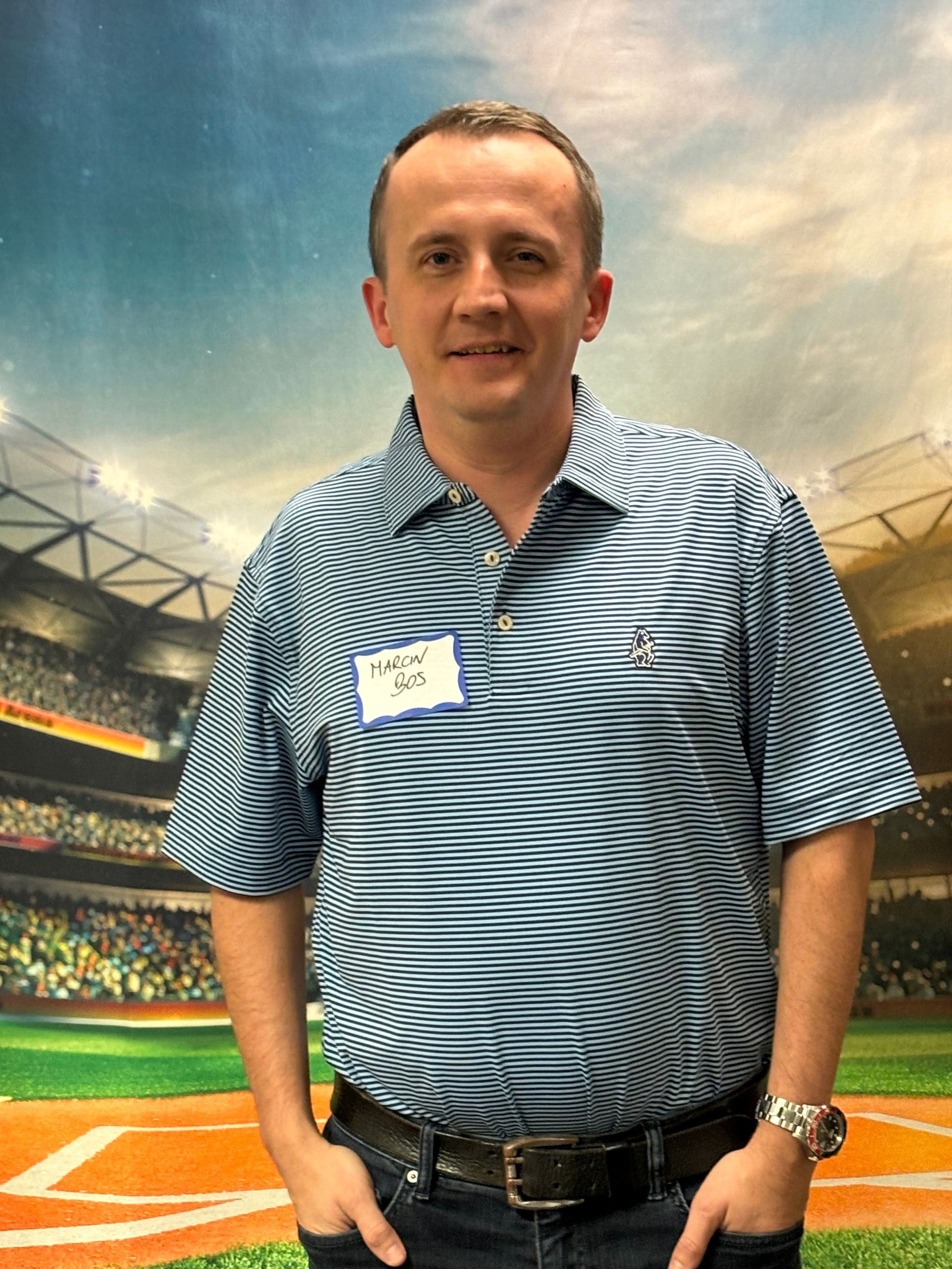 A man wearing a name tag is standing in front of a baseball field