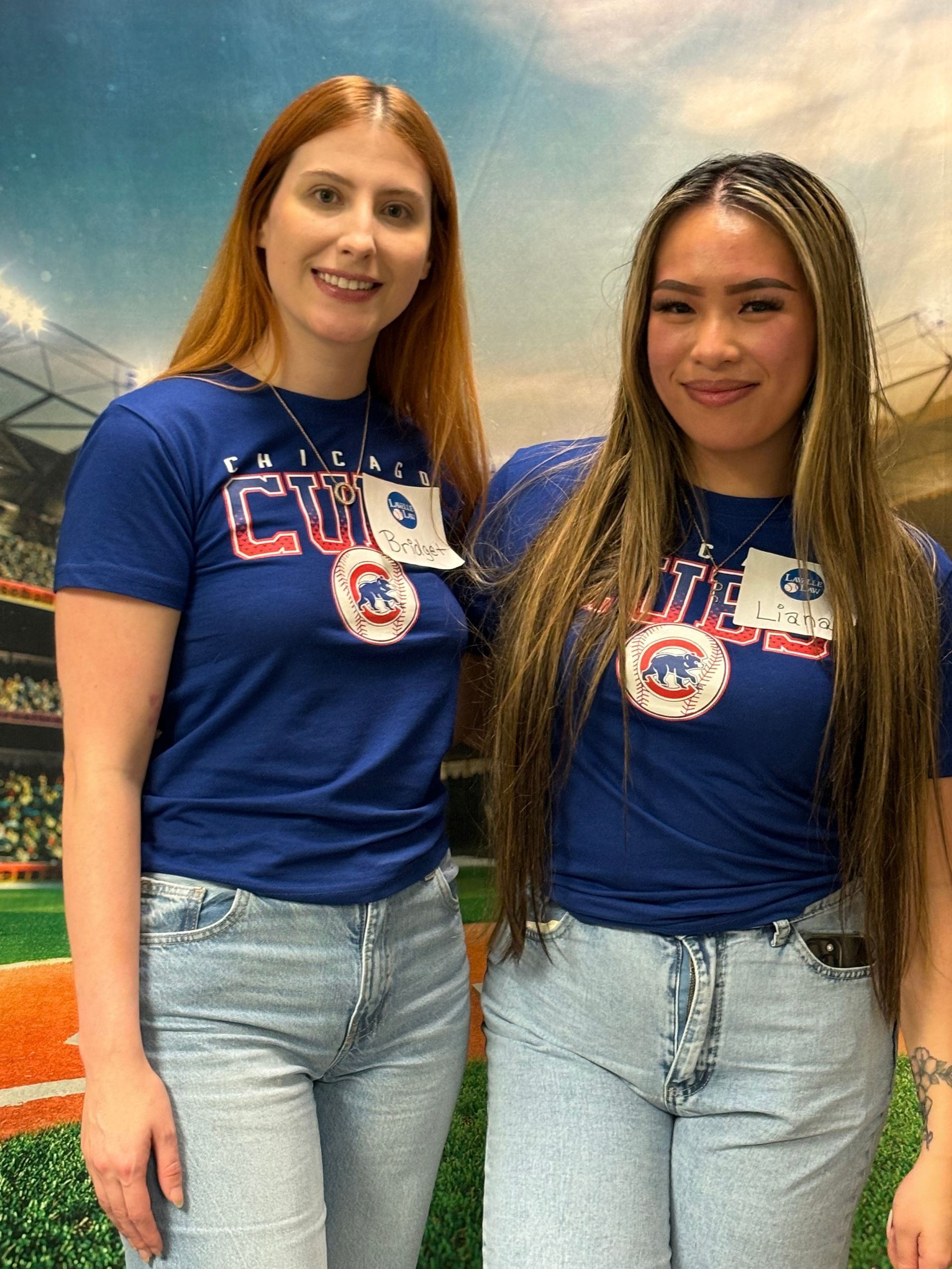 Two women wearing chicago cubs shirts are posing for a picture.