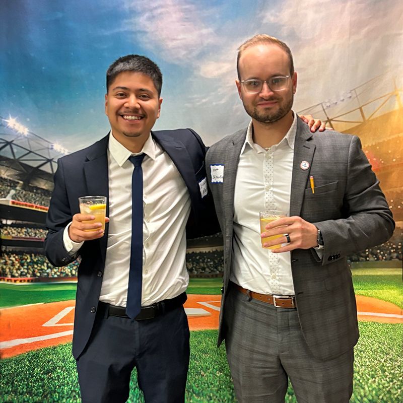 Two men in suits and ties are standing next to each other holding drinks.