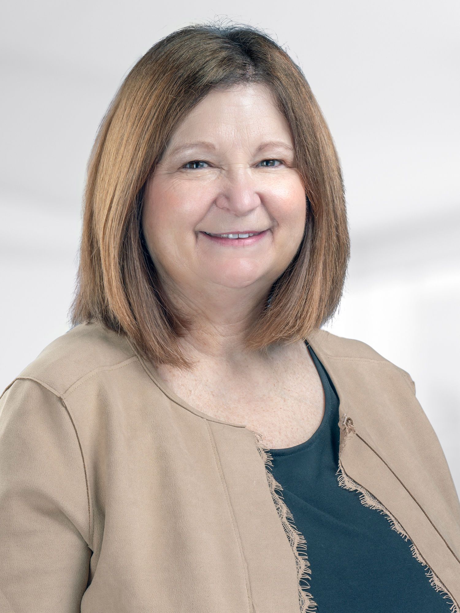 A woman wearing a brown jacket and a black shirt is smiling for the camera.