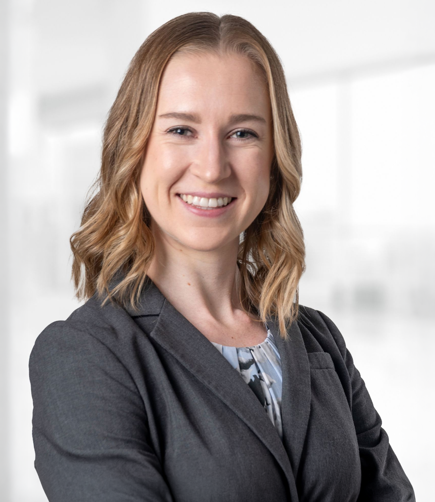 A woman in a suit is smiling for the camera with her arms crossed.