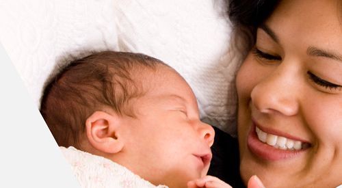 A woman is smiling while holding a baby in her arms.