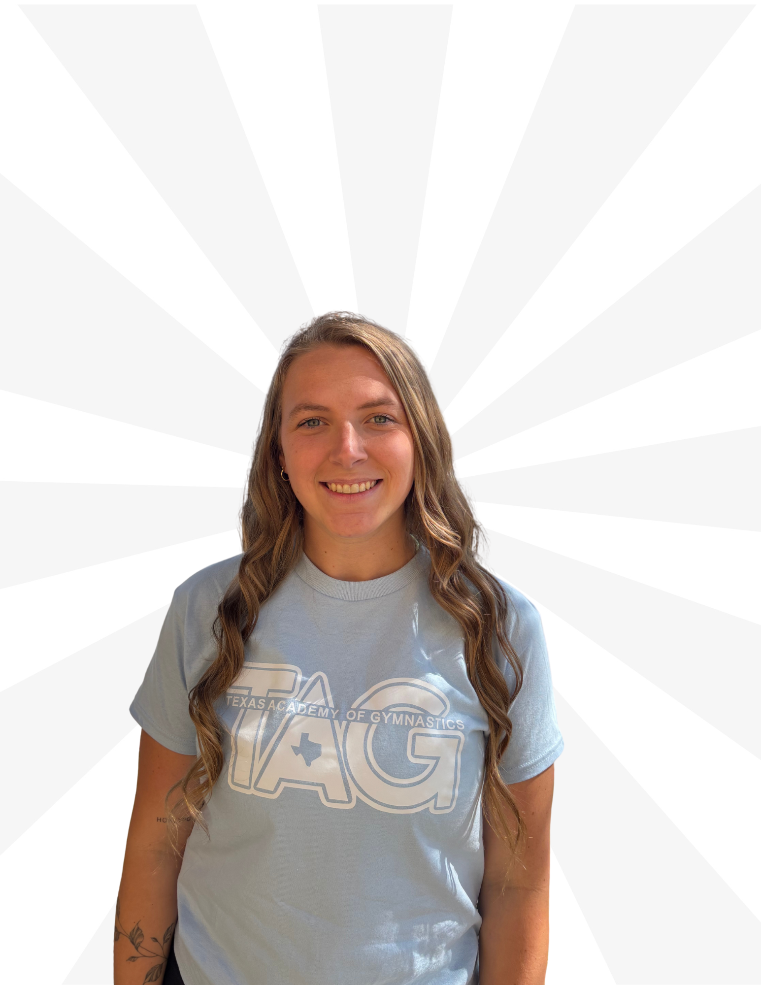 A person with long wavy hair, smiling, wears a light blue t-shirt with 