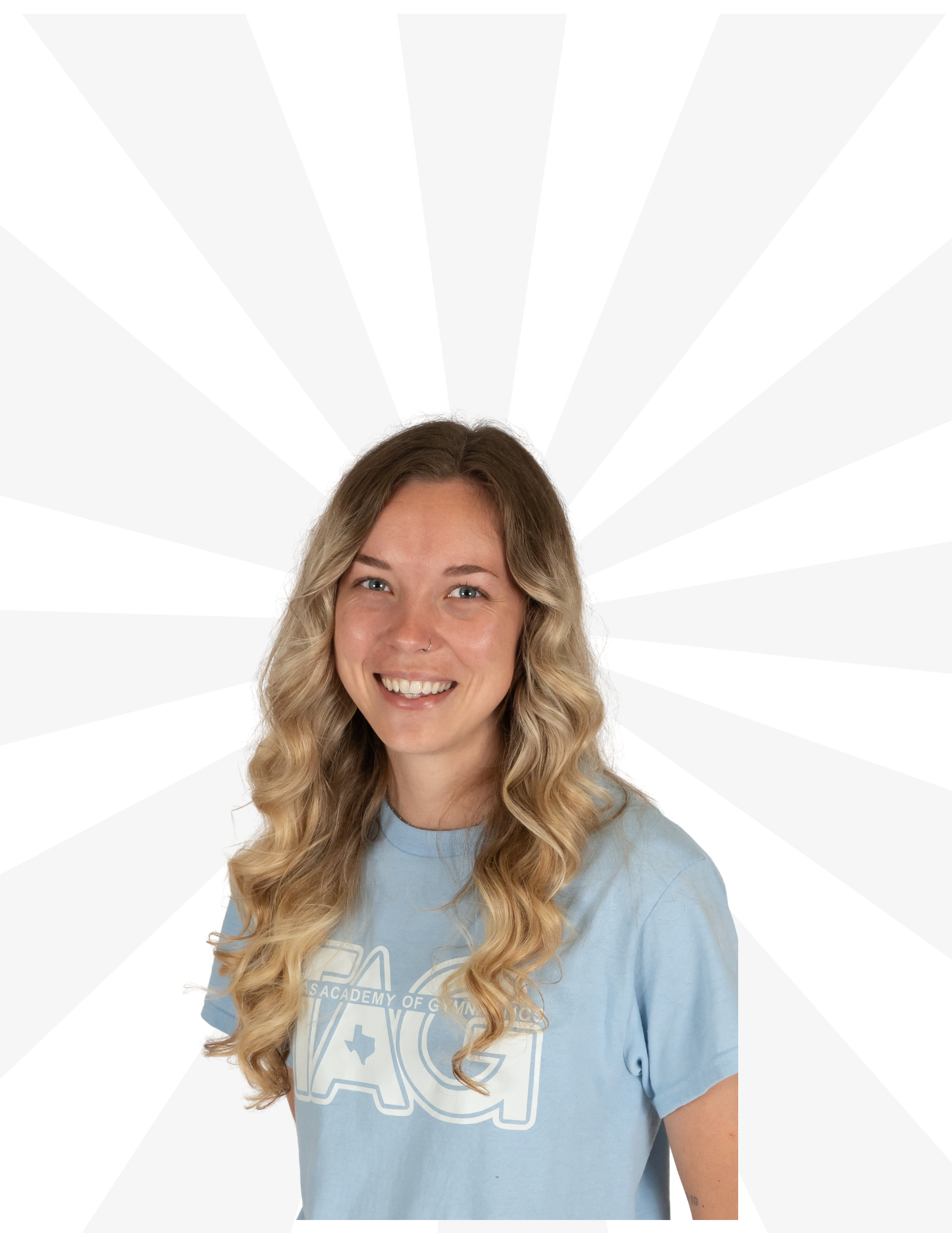 A smiling person with long blonde wavy hair, wearing a light blue t-shirt, centered against a white radiating starburst.