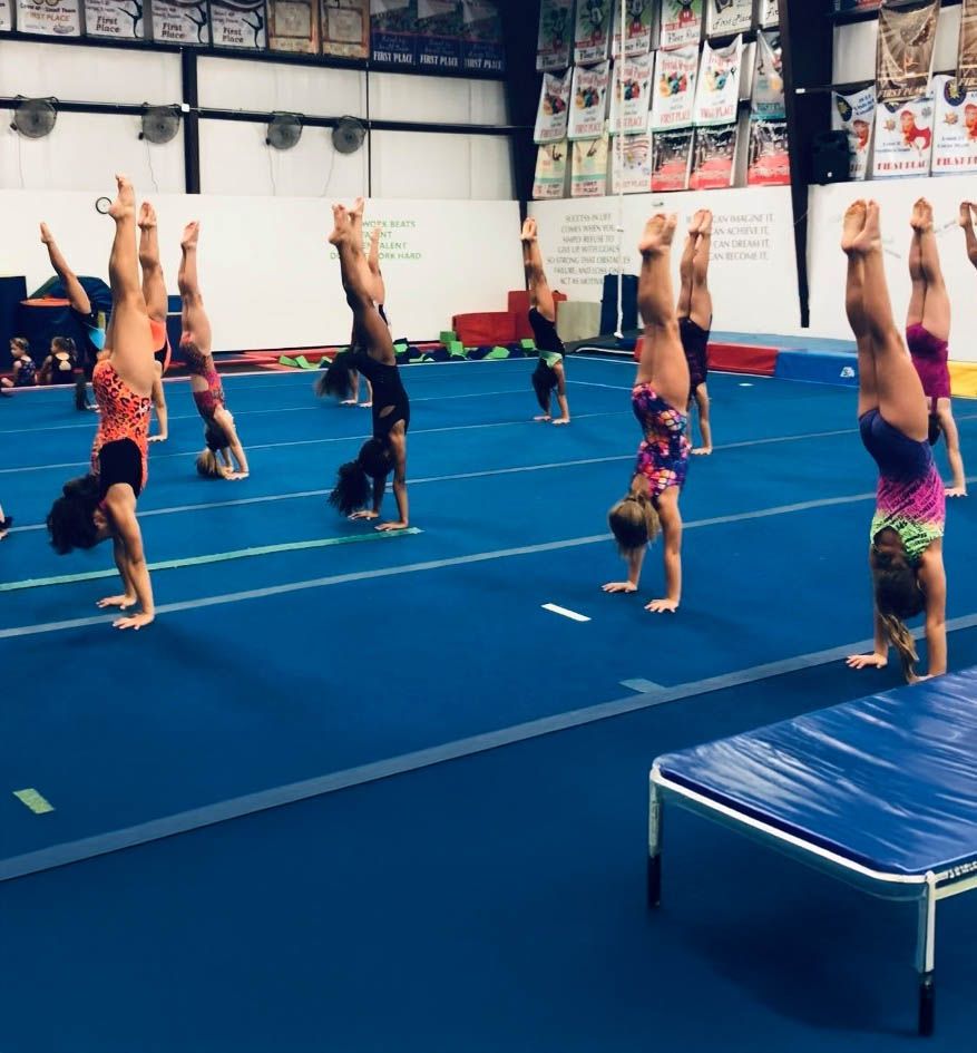 Gymnasts in colorful leotards perform a line of handstands on a blue gym mat.