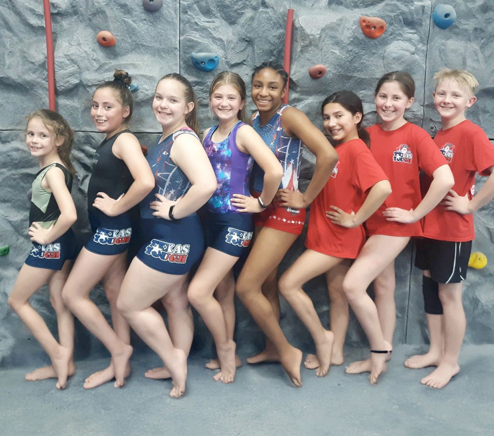 A group of children posing in athletic wear in front of an indoor rock-climbing wall.