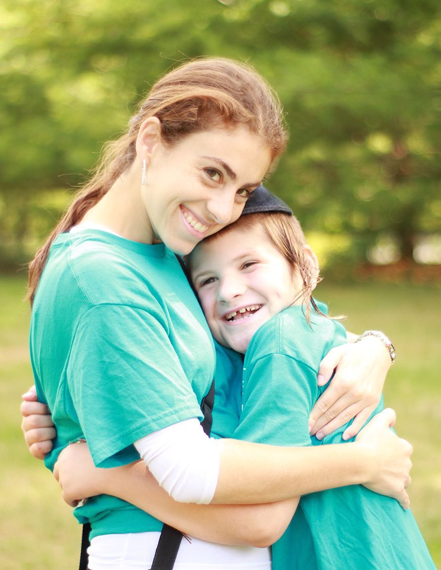 A woman in a green shirt is hugging a young boy in a field.