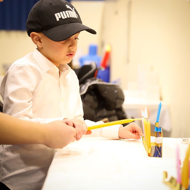 A young boy wearing a black puma hat is lighting a menorah.