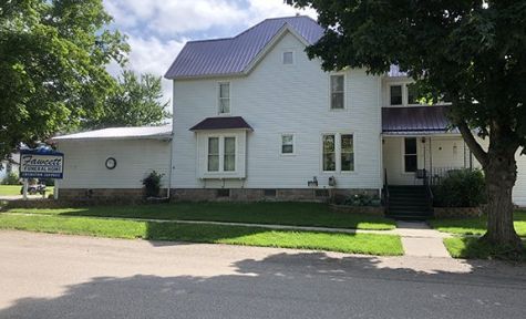 White two-story house with purple roof, front porch, lawn, and large tree White two-story house with purple roof, front porch, lawn, and large tree