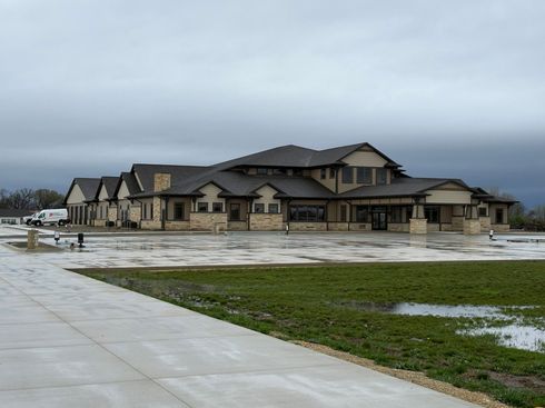 Large tan house with dark roof on a wet, grassy lot