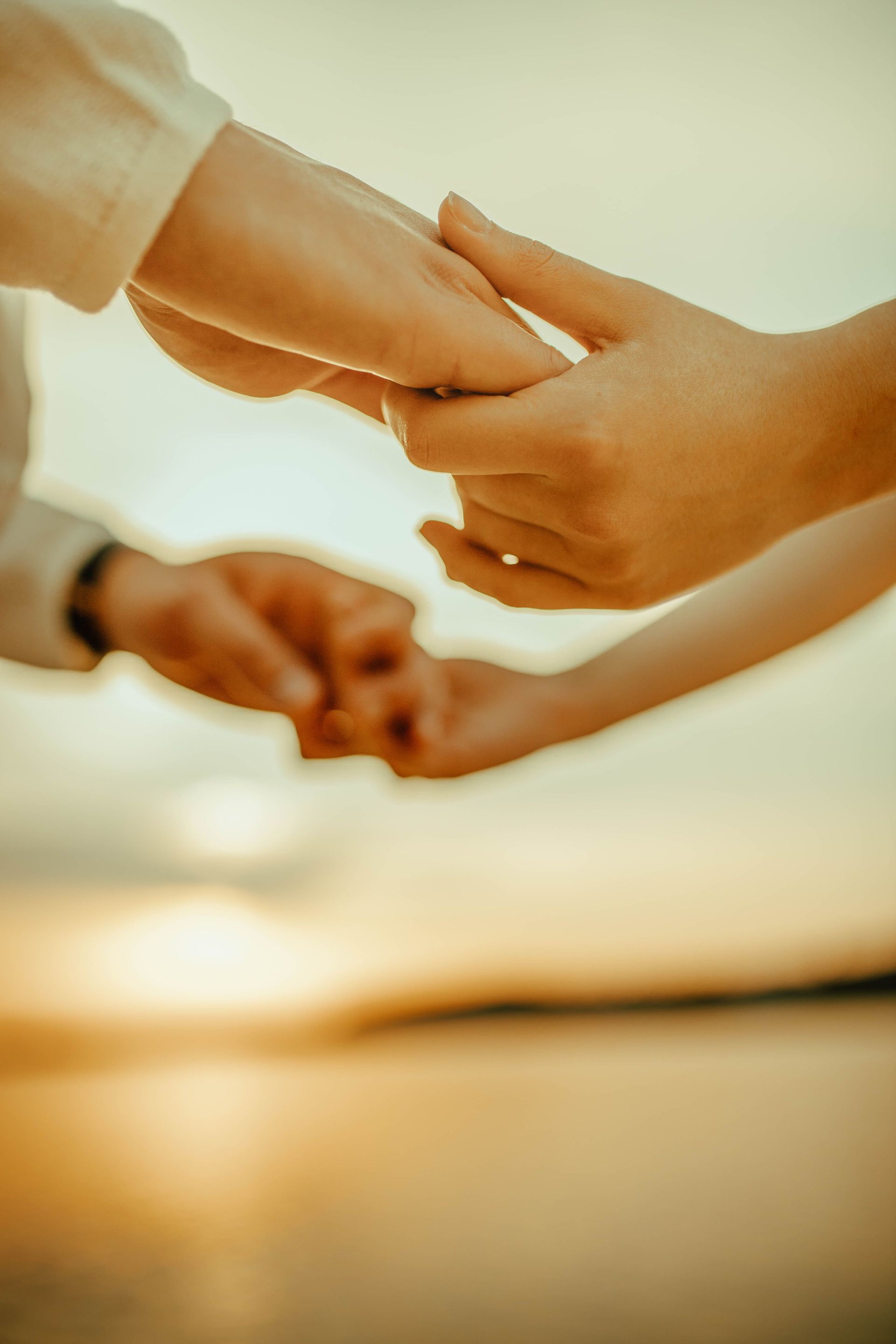 Hands joined in a circle against a warm sunset sky over water