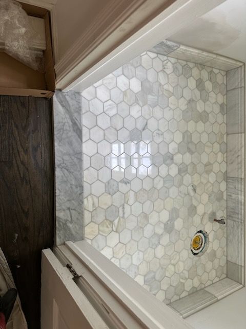 A bathroom with a shower and a window with a honeycomb tile floor.