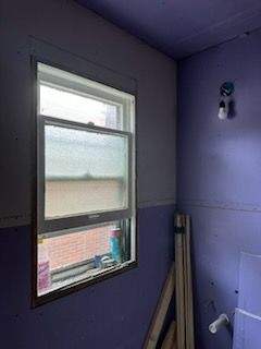 There is a window in the corner of a room with purple walls.