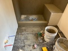 A bathroom under construction with a shower and a bucket of cement on the floor.