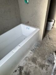 A white bathtub is sitting on a concrete floor in a bathroom.