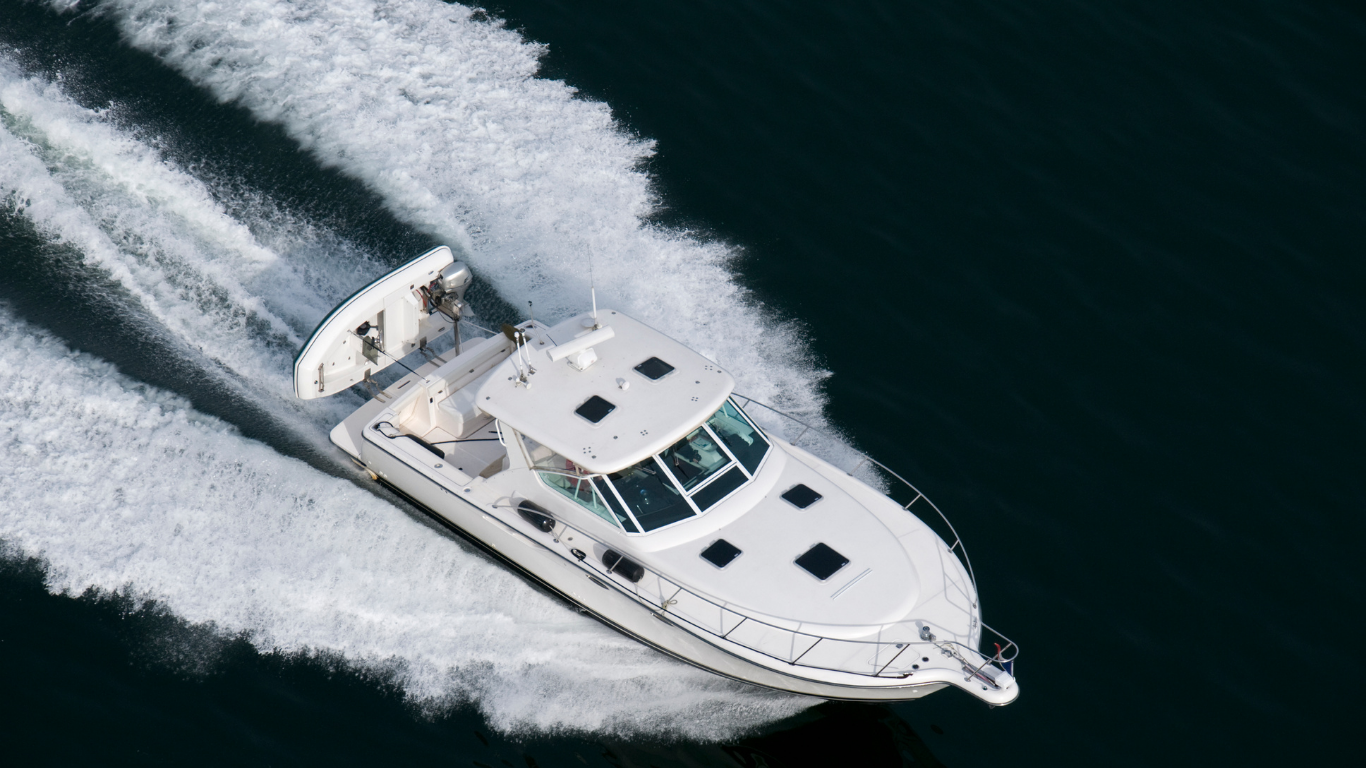 White yacht speeding across dark water, leaving a foamy wake.