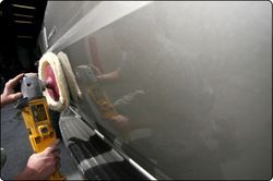 Worker polishing a car door with a buffer, creating a glossy reflection.