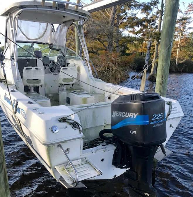 White fishing boat on water with a Mercury 225 outboard motor and covered helm, viewed from the stern
