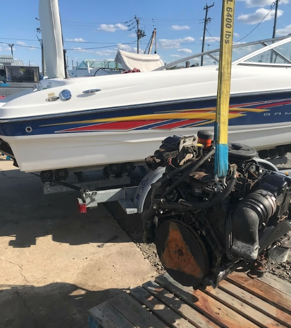 Damaged boat engine on a trailer beside a white speedboat at a marina