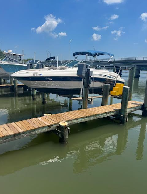 White and navy boat docked at a marina beside a wooden floating pier under a blue sky.