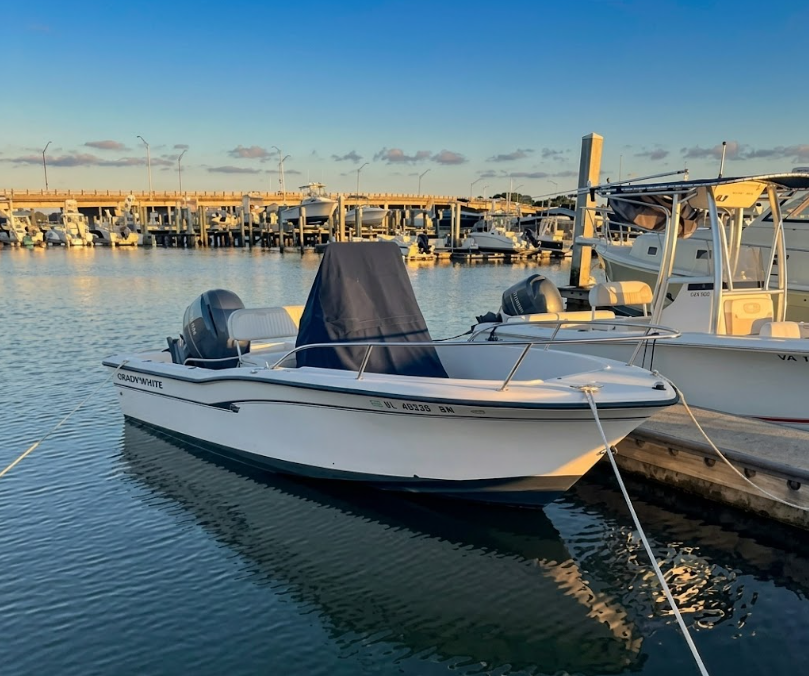 White motorboat docked at a marina at sunset, with calm water and other boats in the background