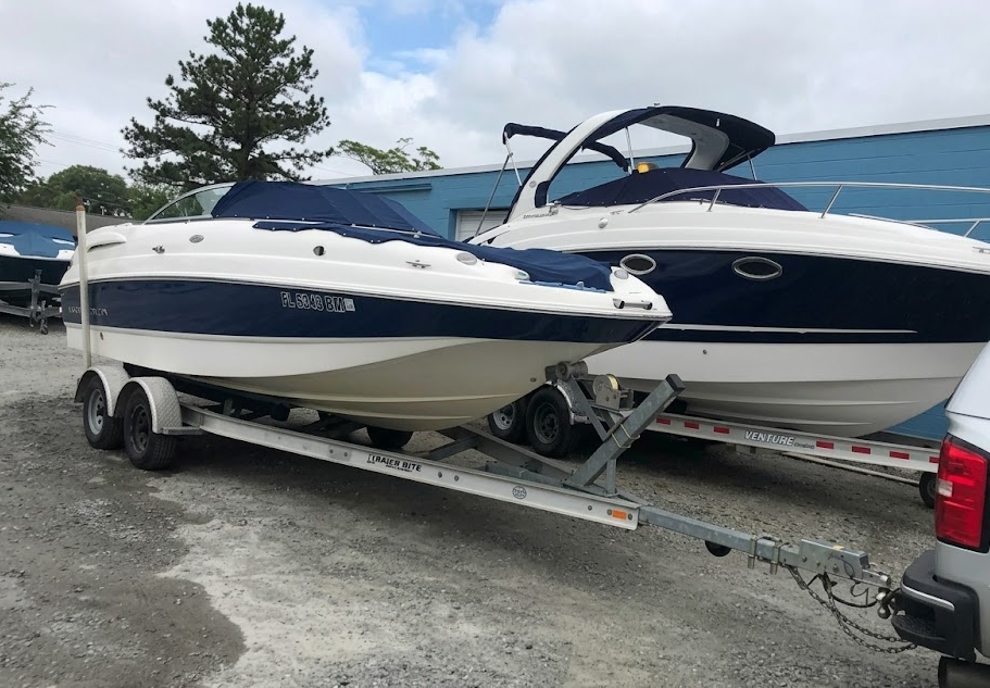 Two white-and-blue motorboats on trailers in a gravel lot under cloudy skies