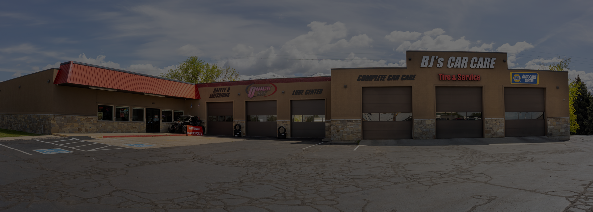 Low brick commercial building with a red roof and large front windows under a cloudy sky | BJ's Car Care