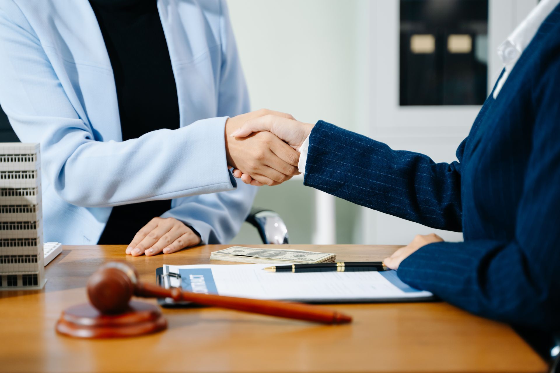 Client shaking hands with a property tax lawyer over real estate contract and gavel on desk.