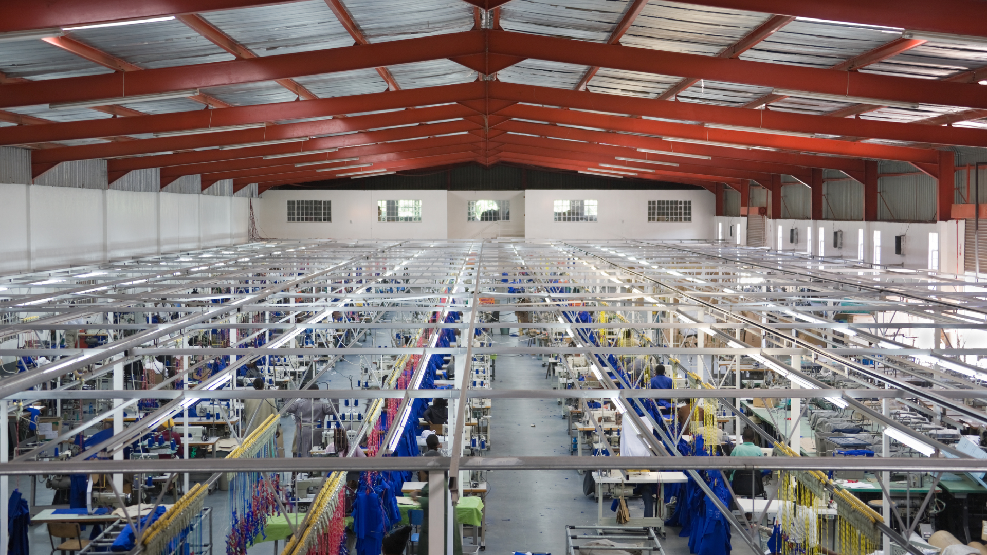 Interior view of a large manufacturing facility with a metal framework supporting production lines; workers are visible below.