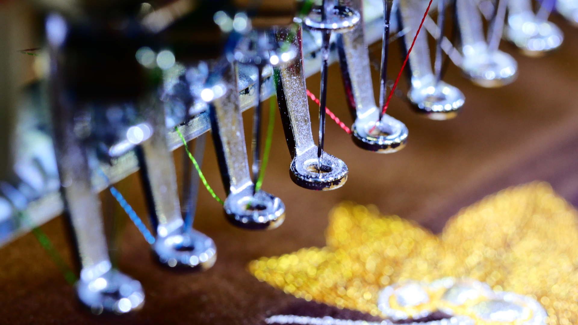 Close-up of embroidery machine needles with colorful threads, stitching a floral design.