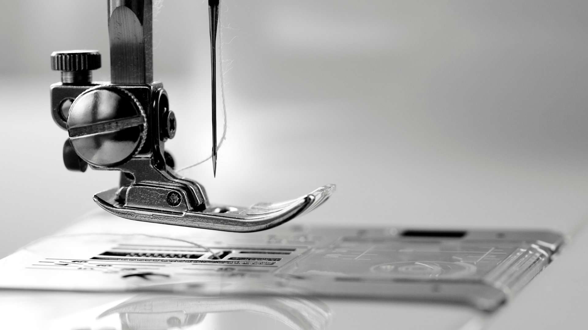 Close-up of a sewing machine needle and presser foot with thread, focused on the needle piercing fabric.