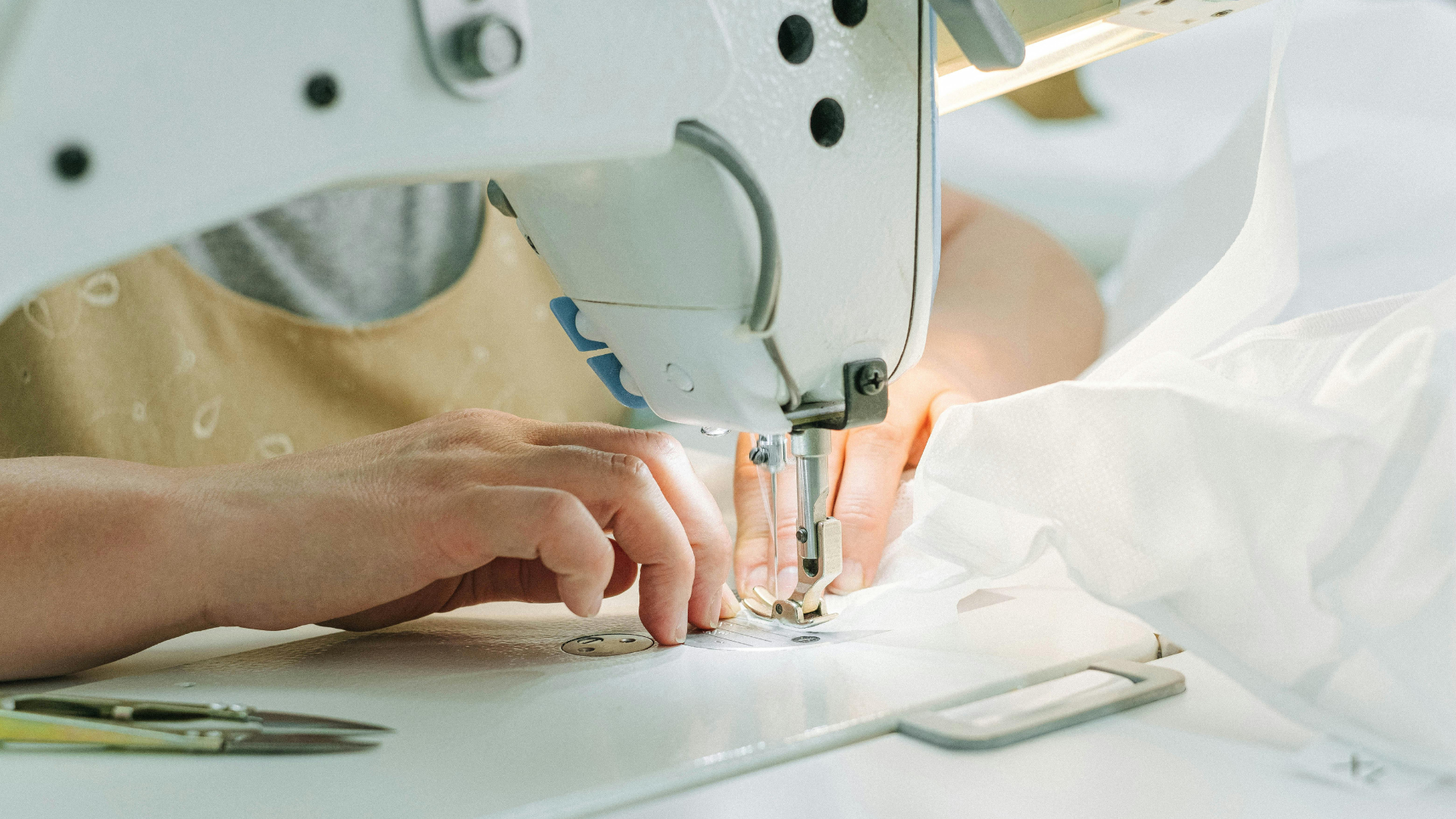 Person using a sewing machine, stitching white fabric. Hands are visible, focused on the needle.