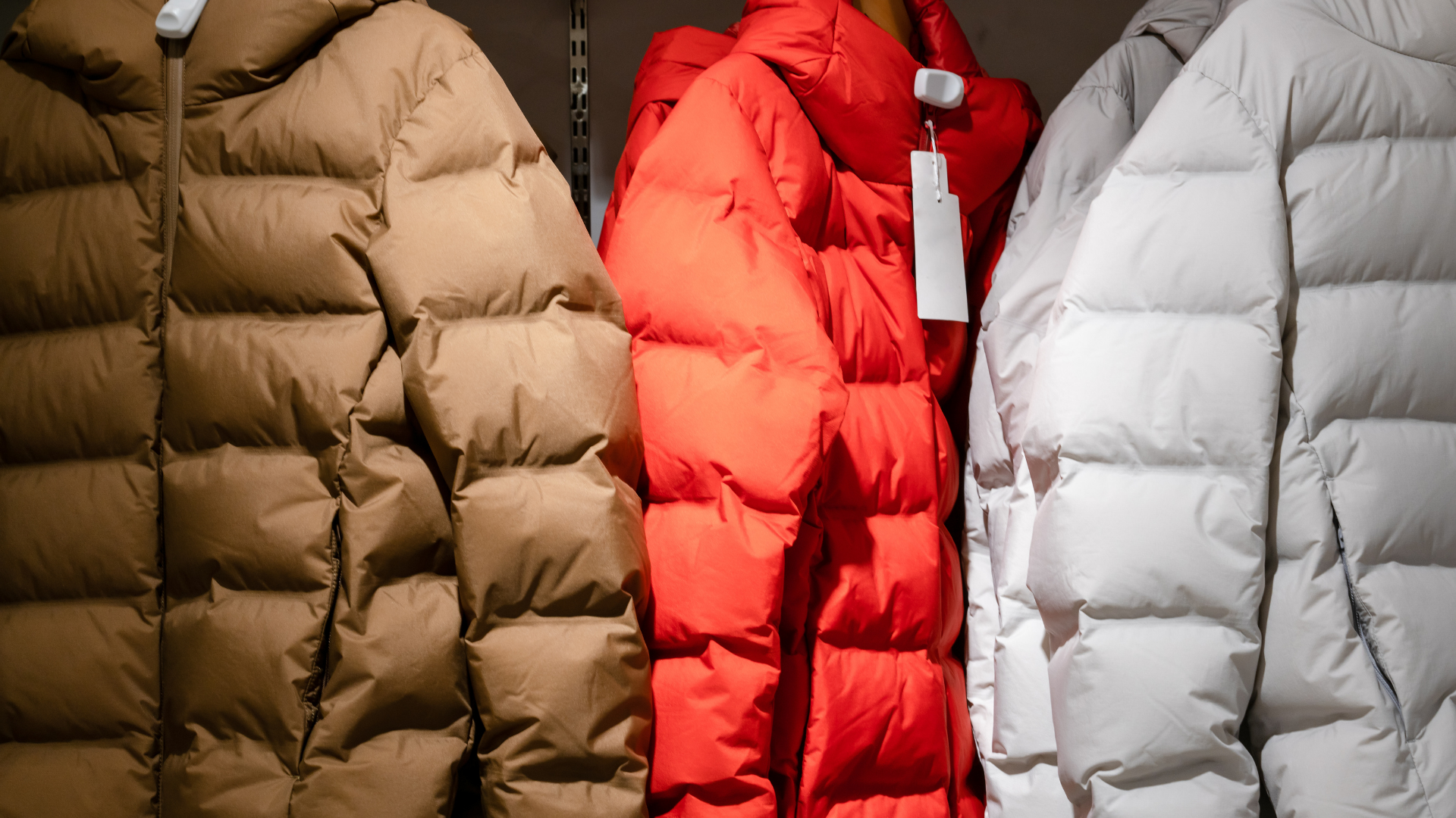 Three puffy winter coats in brown, red, and white hanging on a rack.
