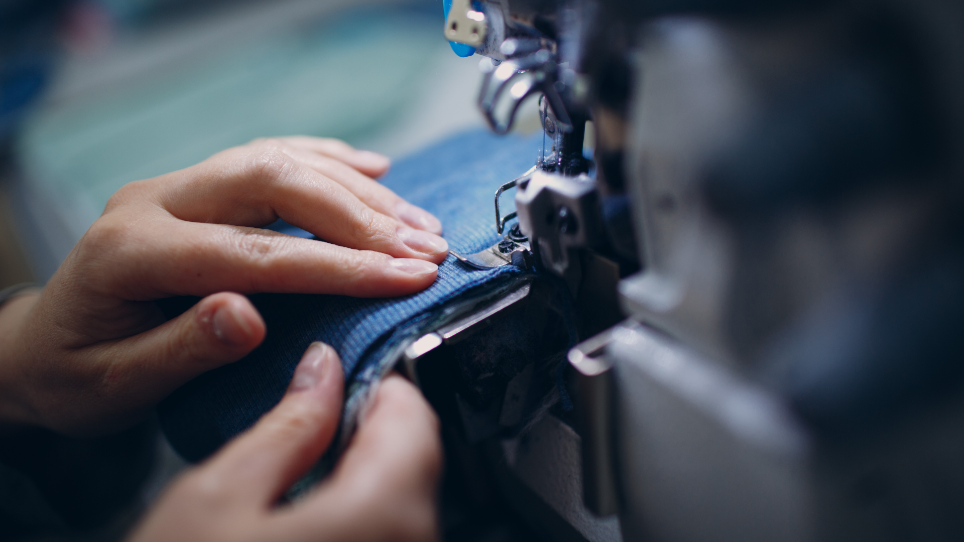 Hands sewing blue denim fabric on a sewing machine.