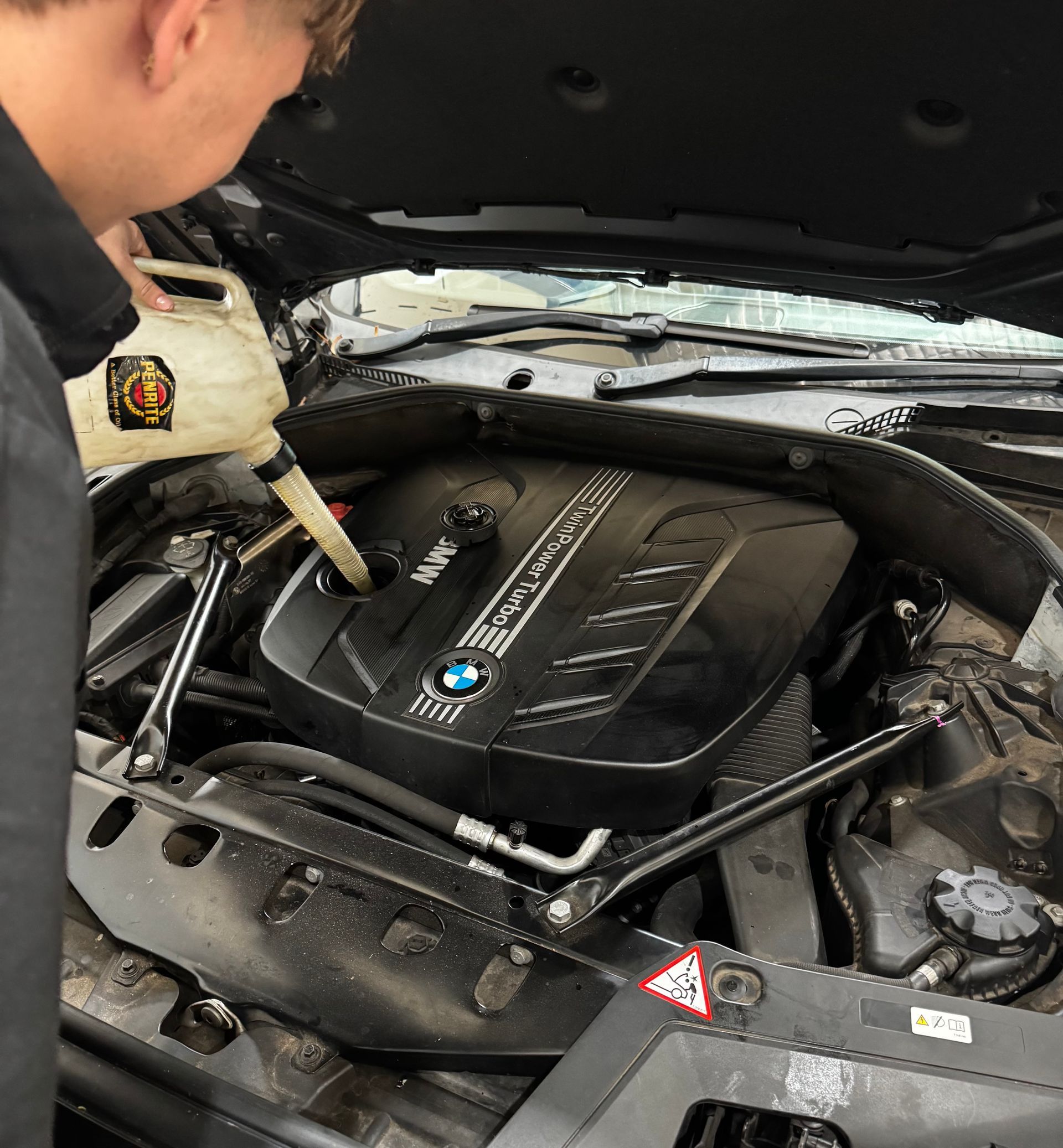 Mechanic Pouring Fluid Into a Bmw Engine Bay Under an Open Hood — Elite Fleet Auto - Electrics & Mechanical in Cannonvale, Qld