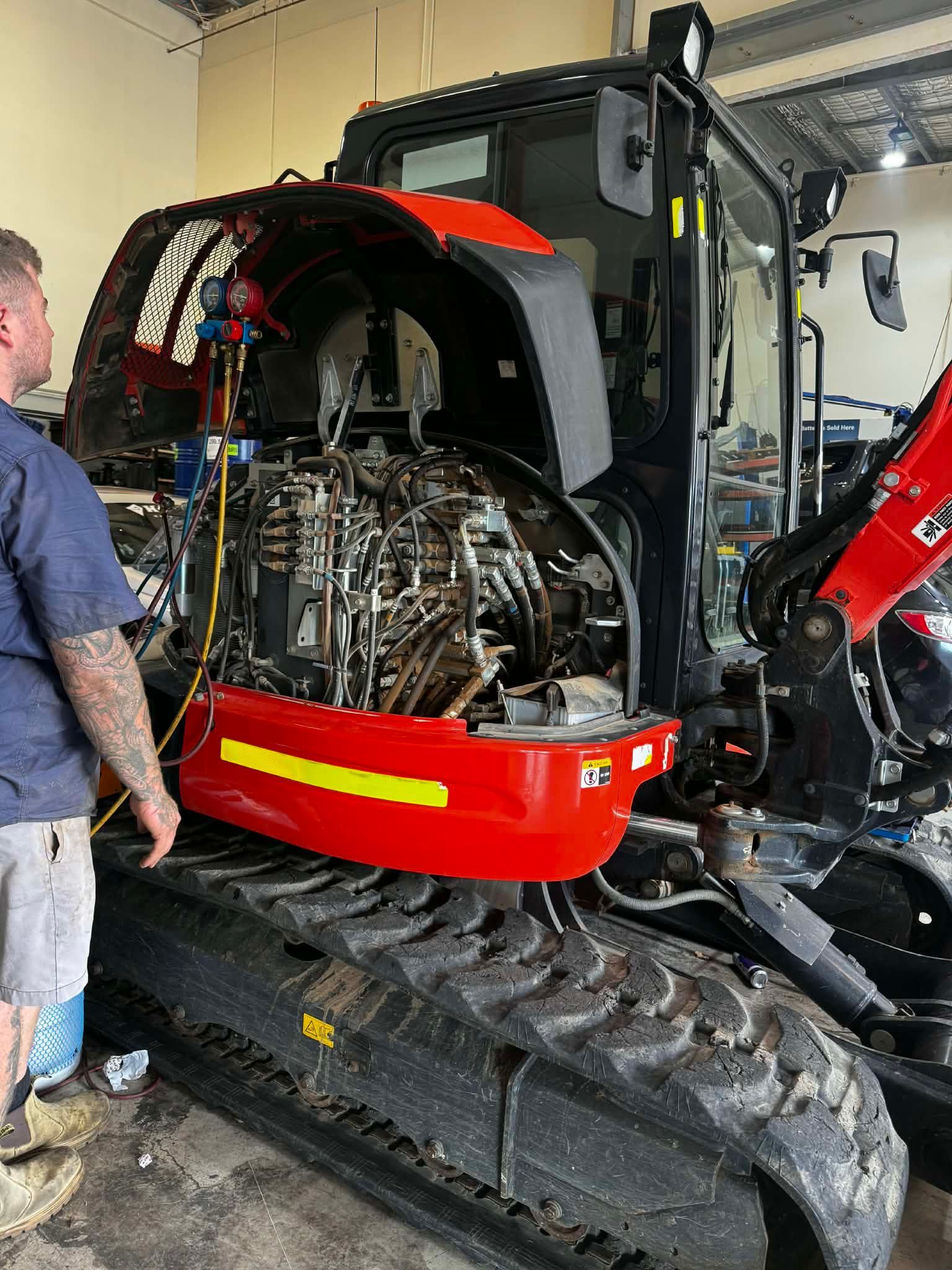A Person Repairs The Internal Hydraulics Of A Red Excavator Parked In A Workshop — Elite Fleet Auto - Electrics & Mechanical in Cannonvale, QLD