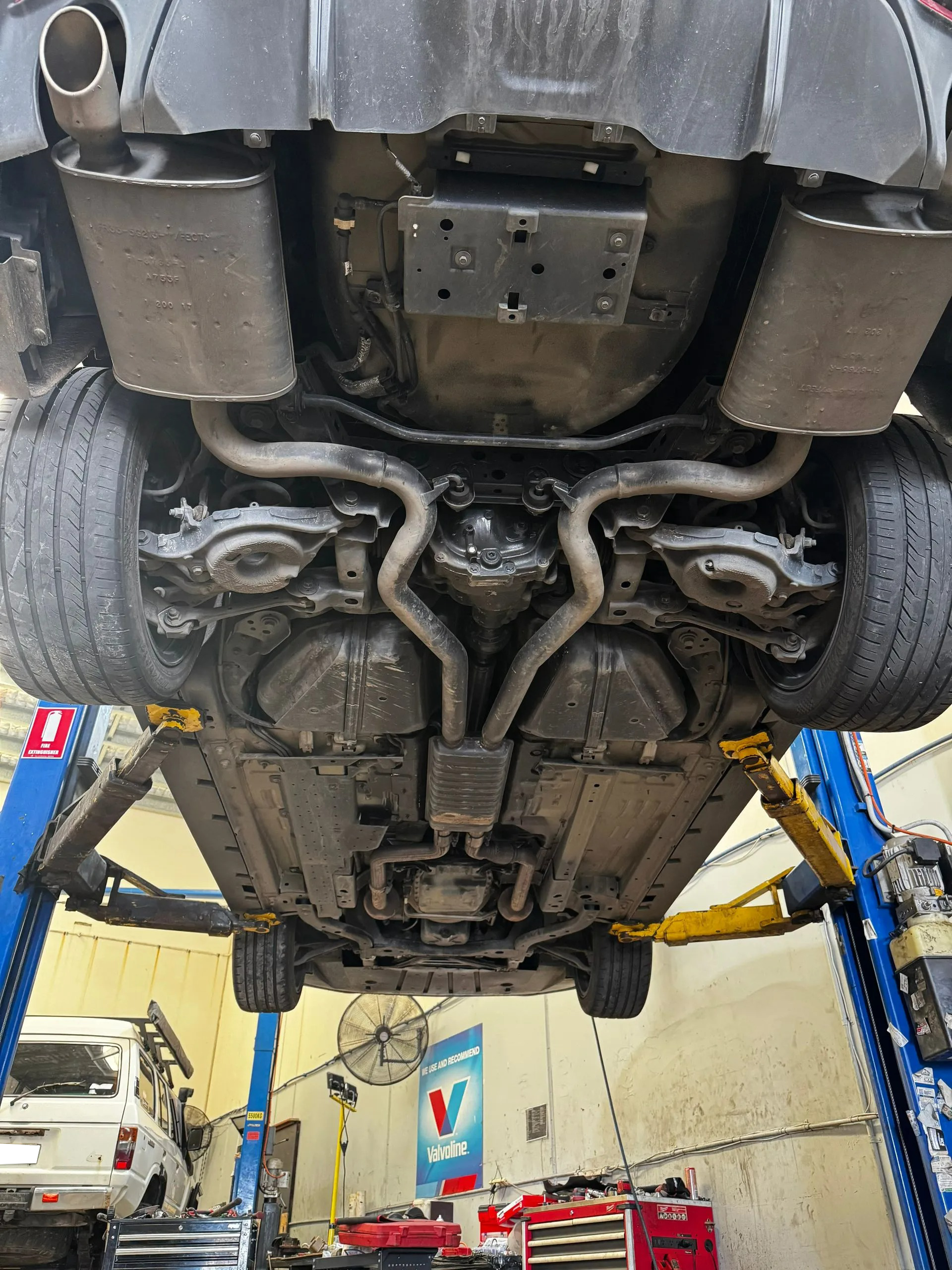 A Vehicle Raised On A Lift In A Shop, Showing Its Exhaust System — Elite Fleet Auto - Electrics & Mechanical in Cannonvale, QLD