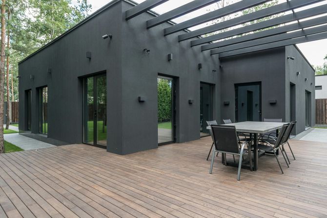 Modern black house with a wooden deck and an outdoor dining set under an attached pergola.