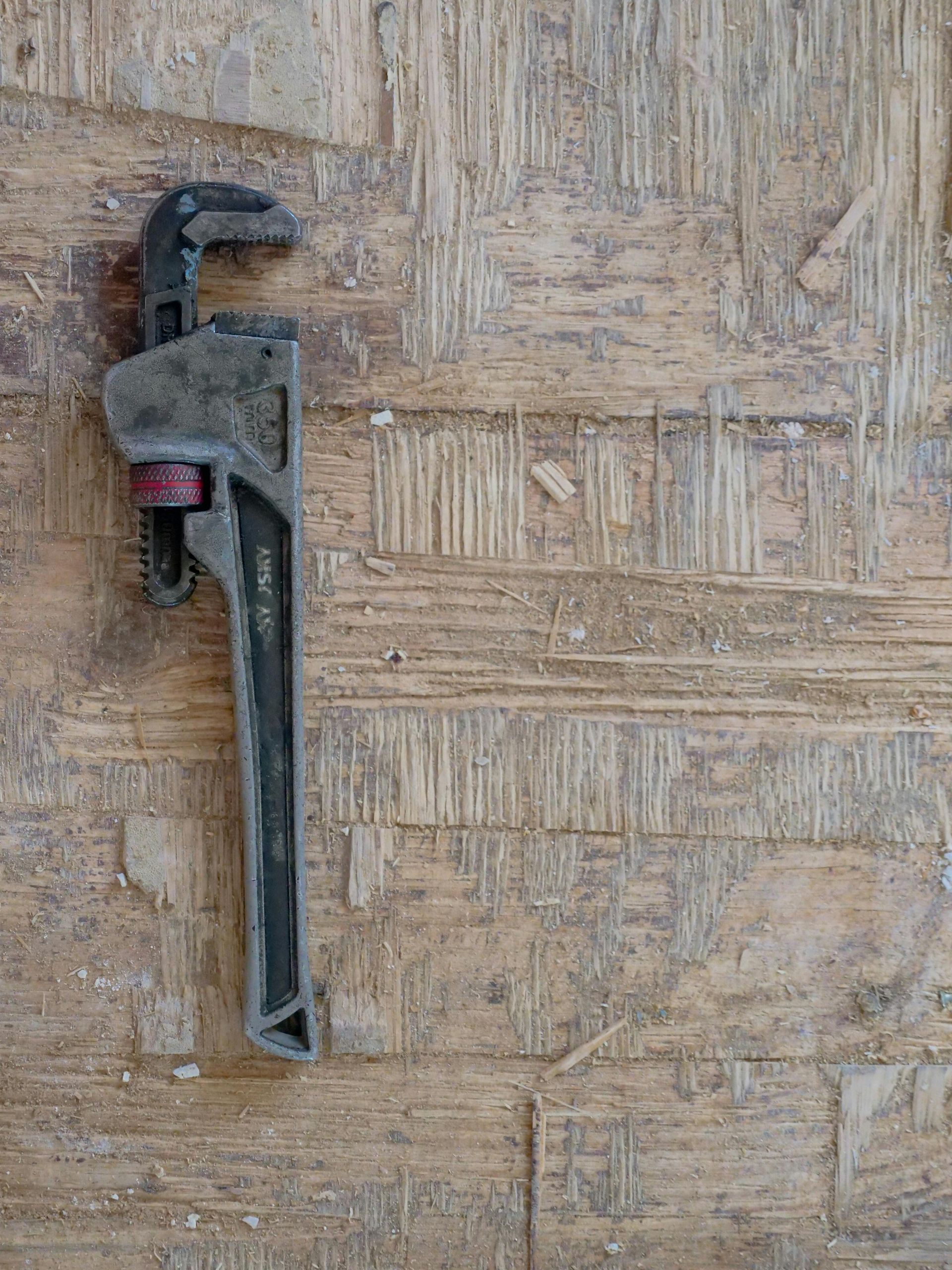 Pipe wrench on a textured, light brown wooden surface.