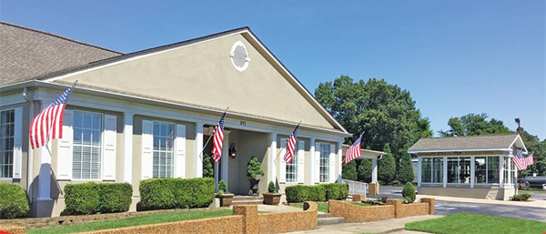 Two beige office buildings with American flags and manicured landscaping on a sunny day