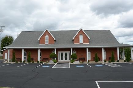 Brick office building with gray roof and white columns, viewed from an empty parking lot.