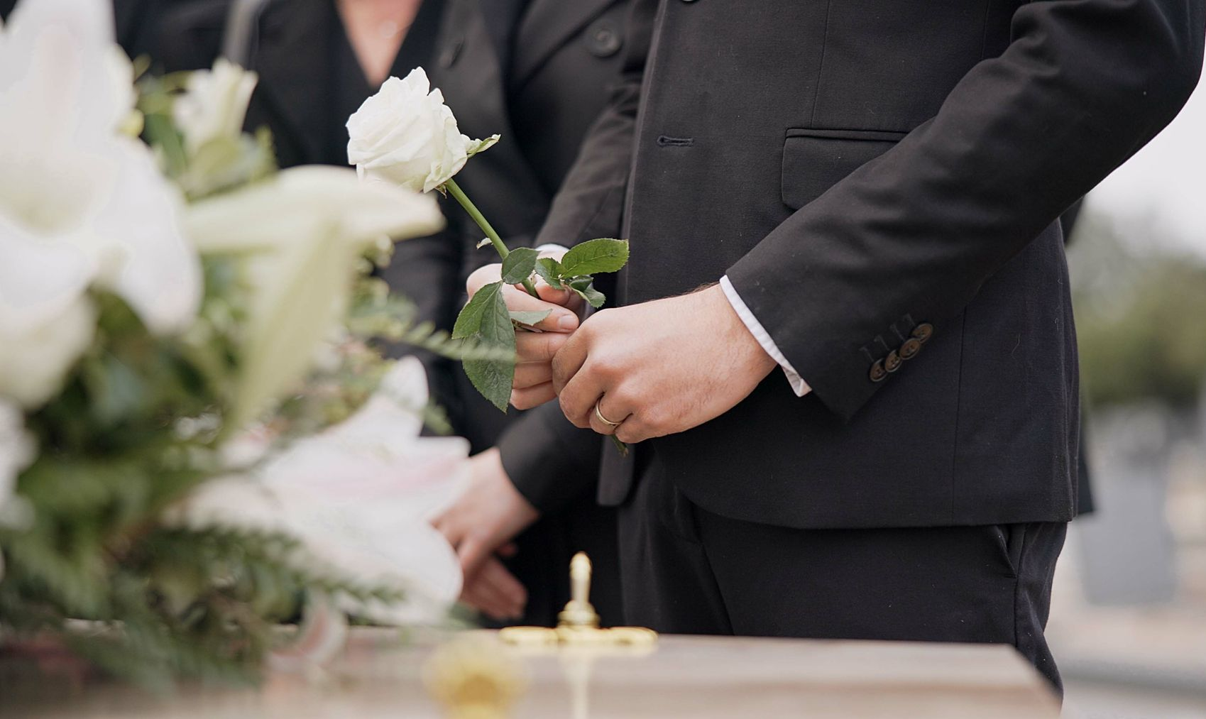 Hands of a couple in black formalwear holding a white rose during a wedding ceremony