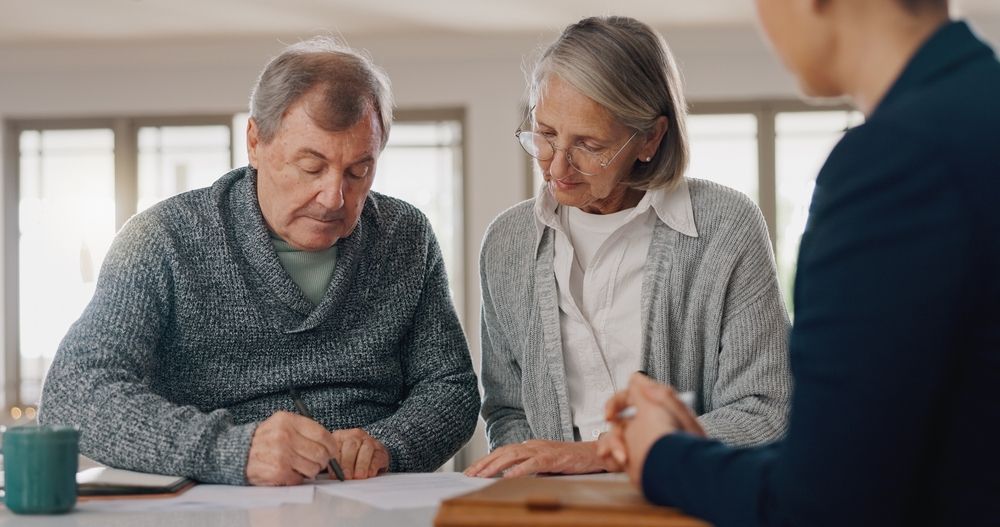 An elderly couple is sitting at a table signing a document.