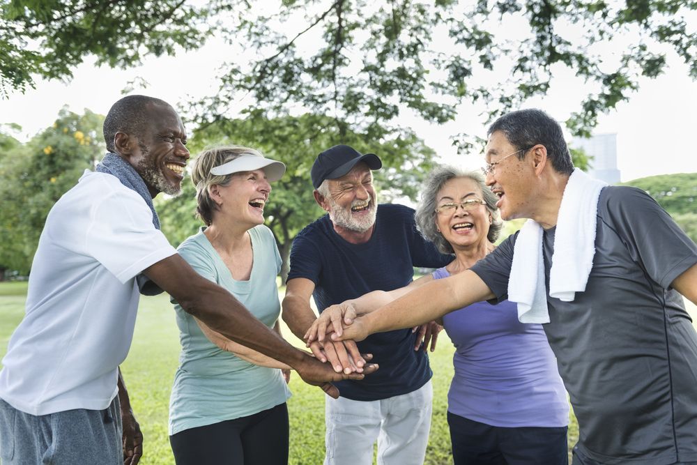 A group of older people are putting their hands together in a park.