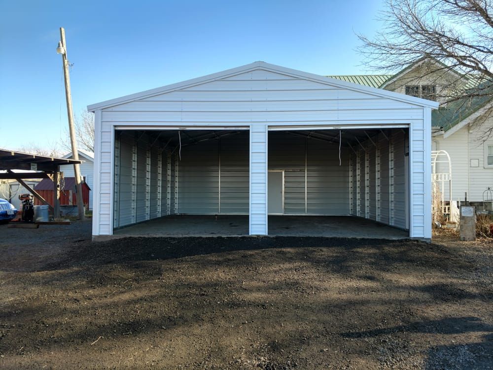 A white garage with two doors is sitting on top of a dirt road.