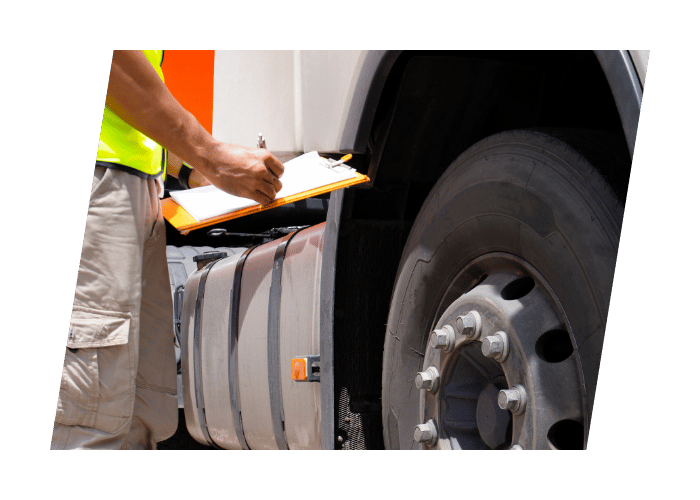 Inspector completing a commercial vehicle safety inspection while recording findings beside a heavy duty truck wheel.