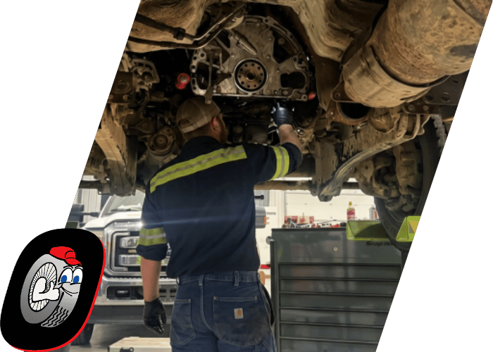 Technician performing diesel transmission or drivetrain repairs beneath a lifted commercial truck.