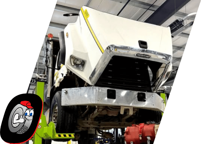 Commercial truck lifted in a repair shop with the hood open for diesel diagnostics and inspection.