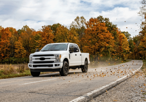 White Ford Super Duty pickup driving through falling autumn leaves on a rural road